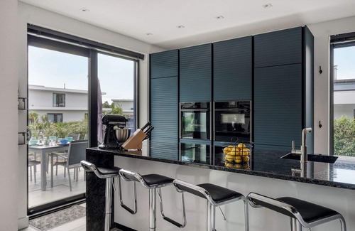 Zeewolde Casa | Detached 6-person villa by the water with a cosy living room featuring a piano and fireplace, modern kitchen with cooking island, and a sunny garden with lounge set.