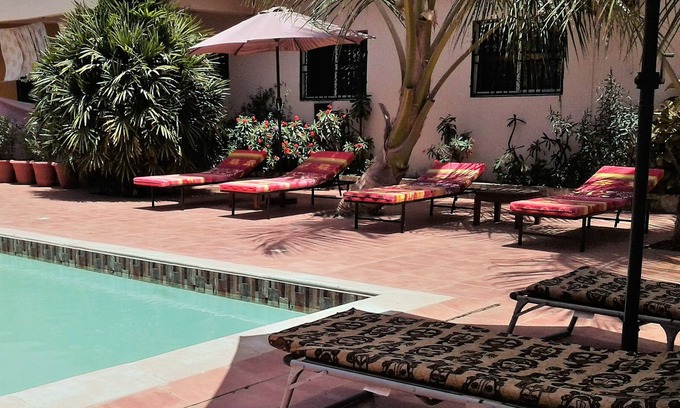 Serrekunda Cama Y Desayuno | Bonita habitación con cama doble junto a la piscina en un jardín tropical.
