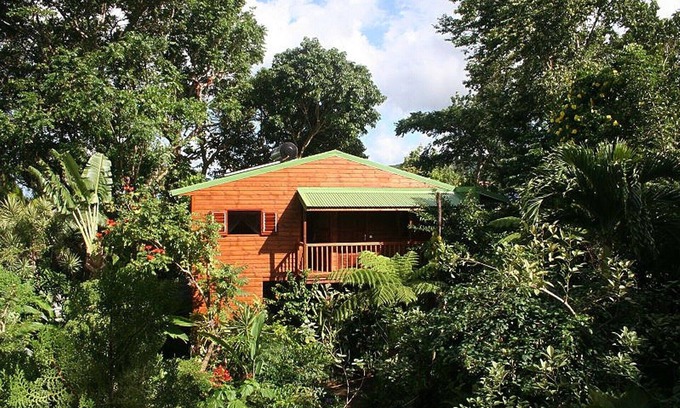 Pointe-Noire Cabaña | Bungalow rojo de madera en un parque con ambiente tropical.